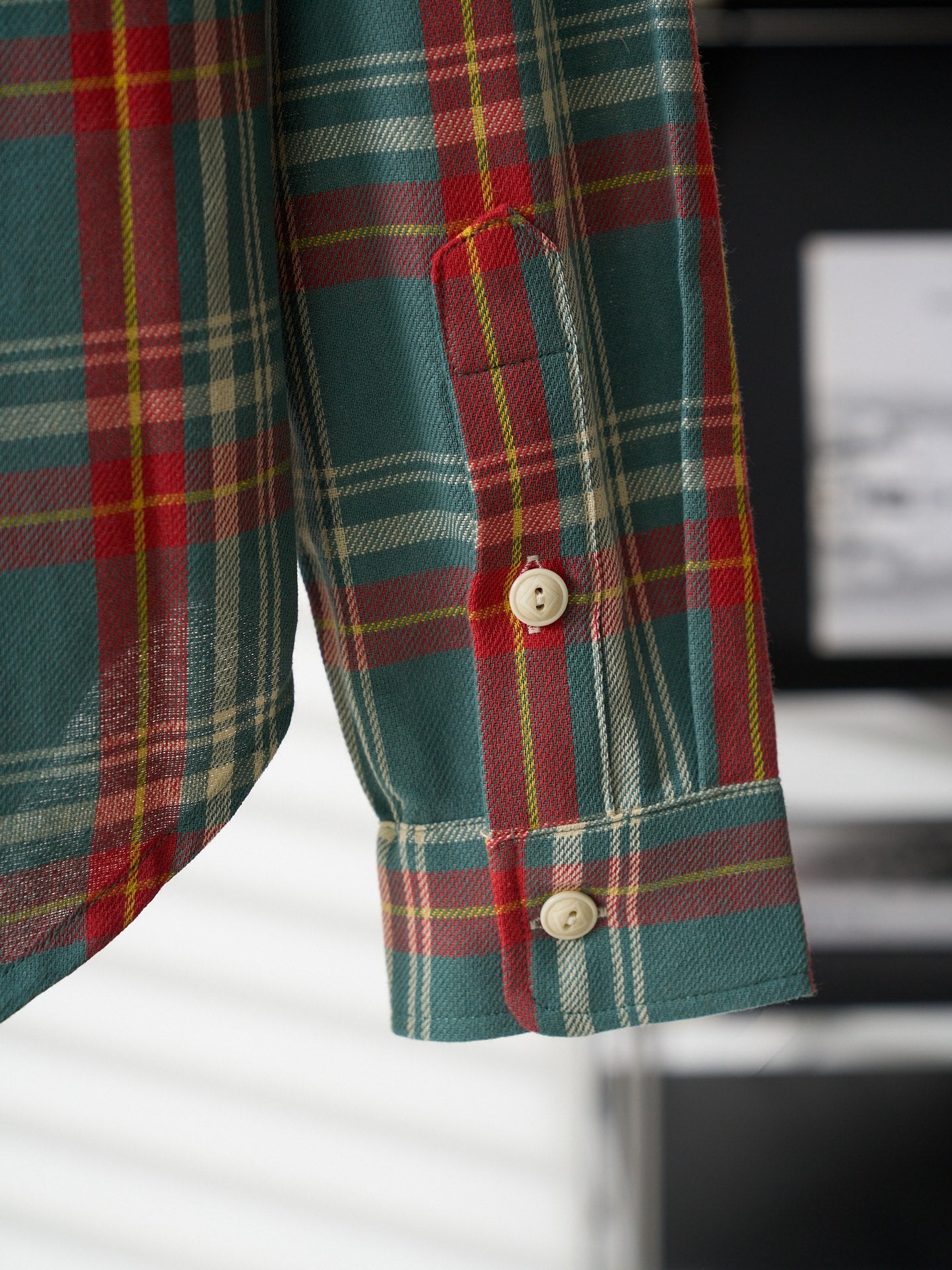 Plaid shirt sleeve cuff detail in teal with red, green, and white stripes