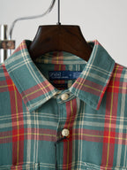 Teal plaid button-up shirt collar and front buttons with a small chest logo patch