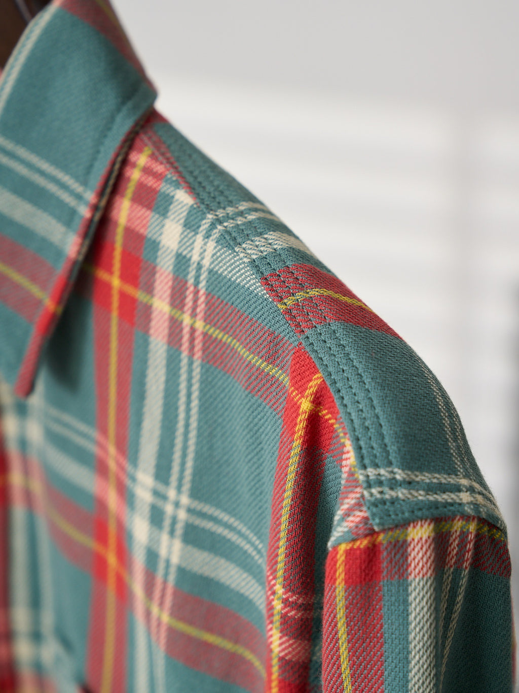 Plaid shirt shoulder seam detail in teal with red, green, and white stripes