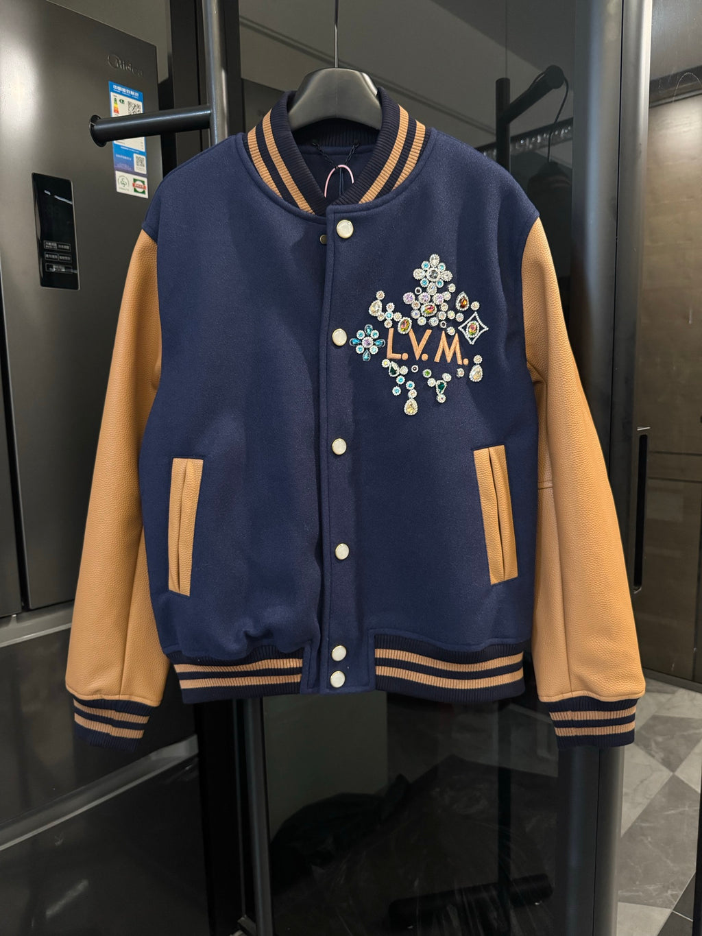 Long varsity jacket in dark navy with tan sleeves, striped rib trim, snap buttons, LV crest