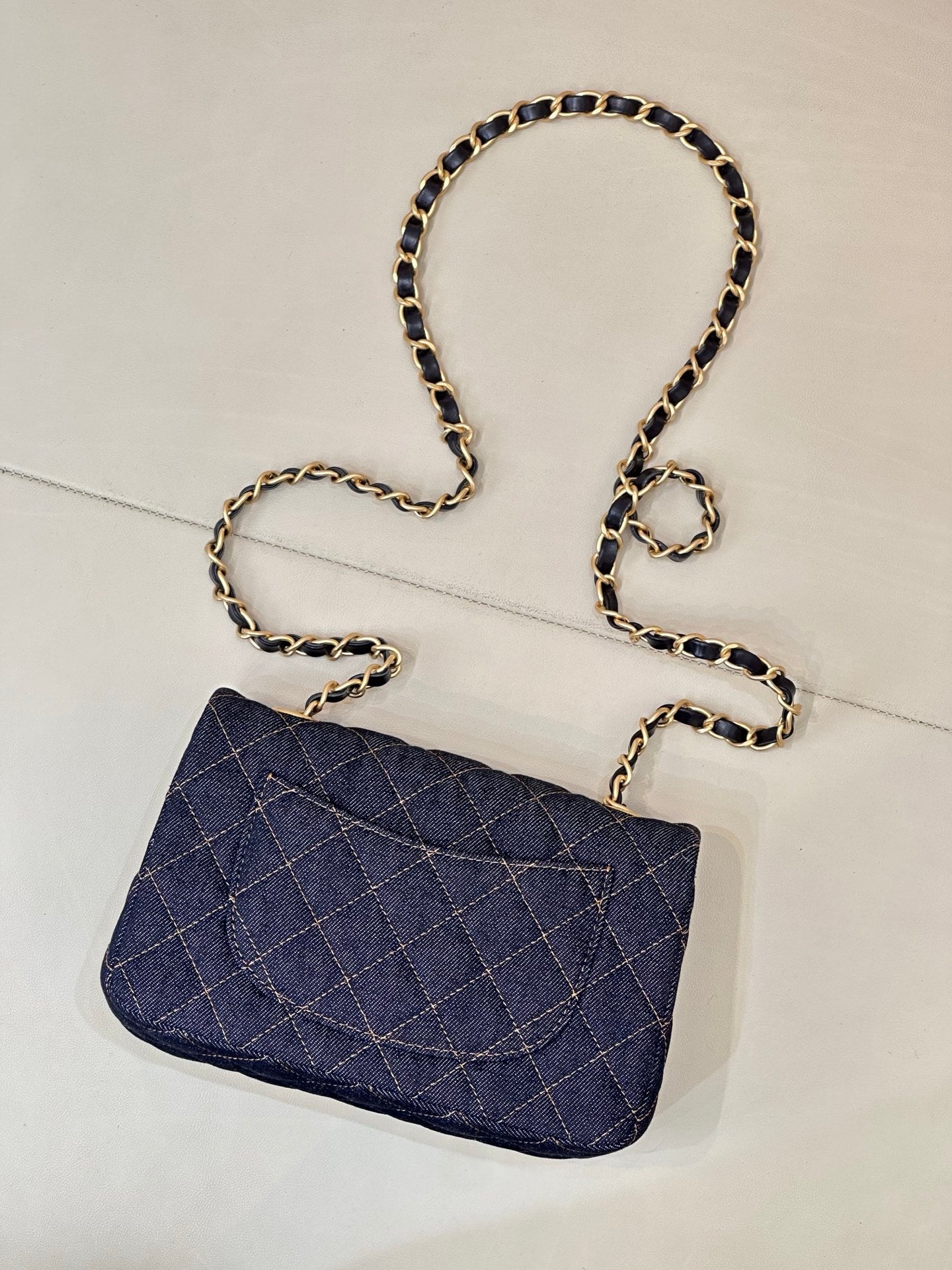 Chanel quilted denim shoulder bag with gold CC logo and chain strap, flat lay.