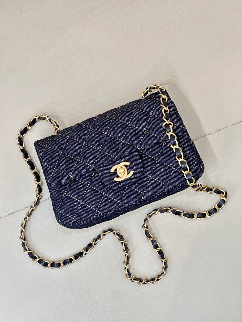 Chanel quilted denim crossbody bag with gold CC logo and curb chain strap.