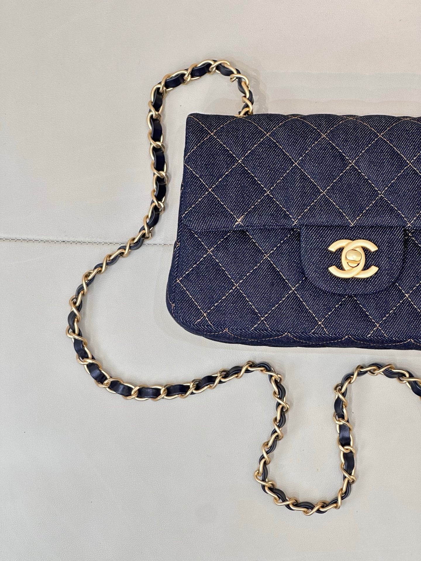 Chanel quilted denim flap bag detail with gold CC logo and chain strap.
