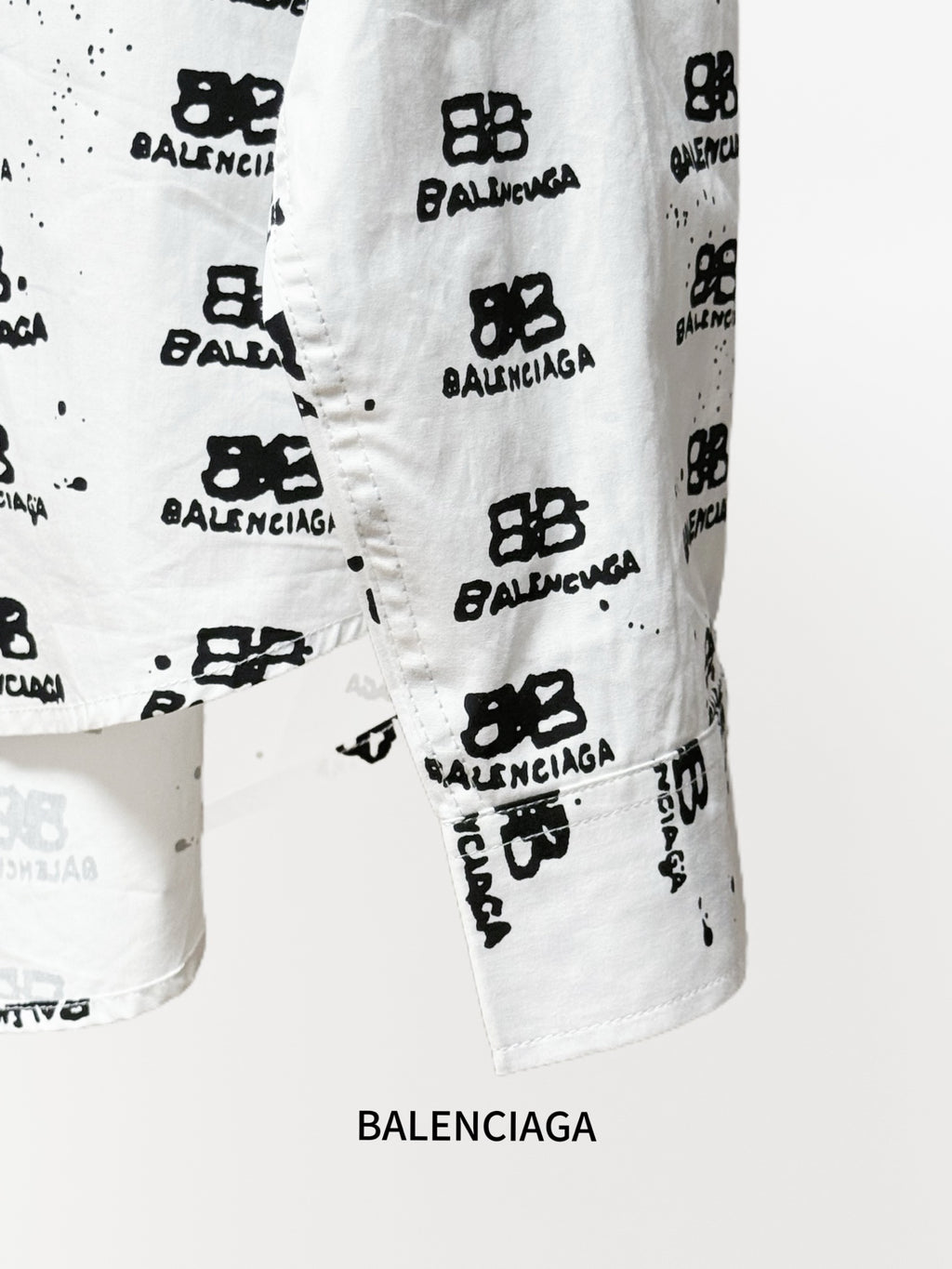 White shirt sleeve hem detail with black logo pattern and visible stitching.