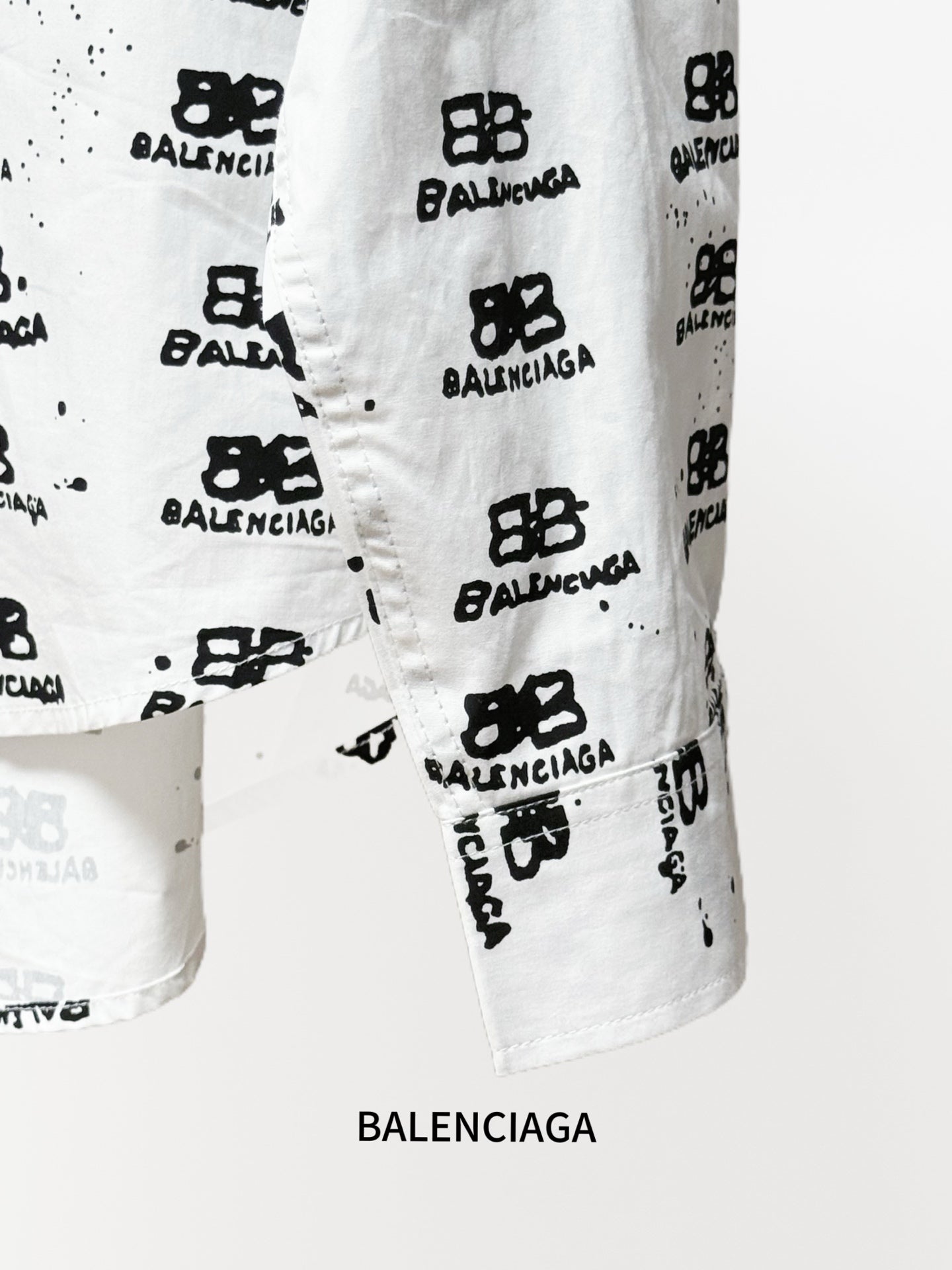 White shirt sleeve hem detail with black logo pattern and visible stitching.