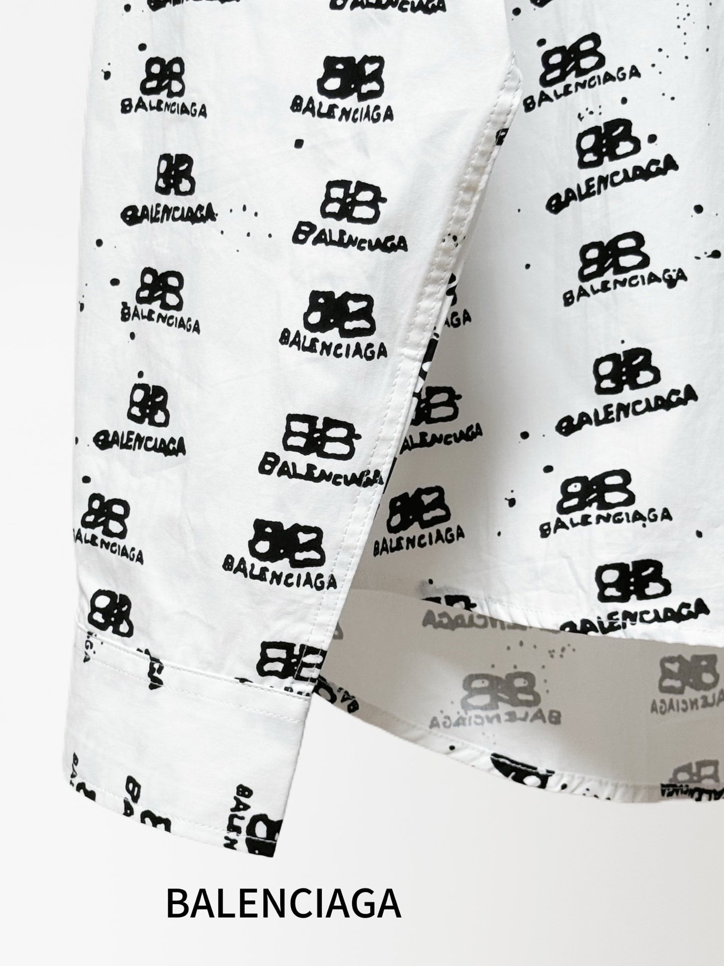 White shirt cuff and side placket detail with black logo pattern and buttons.