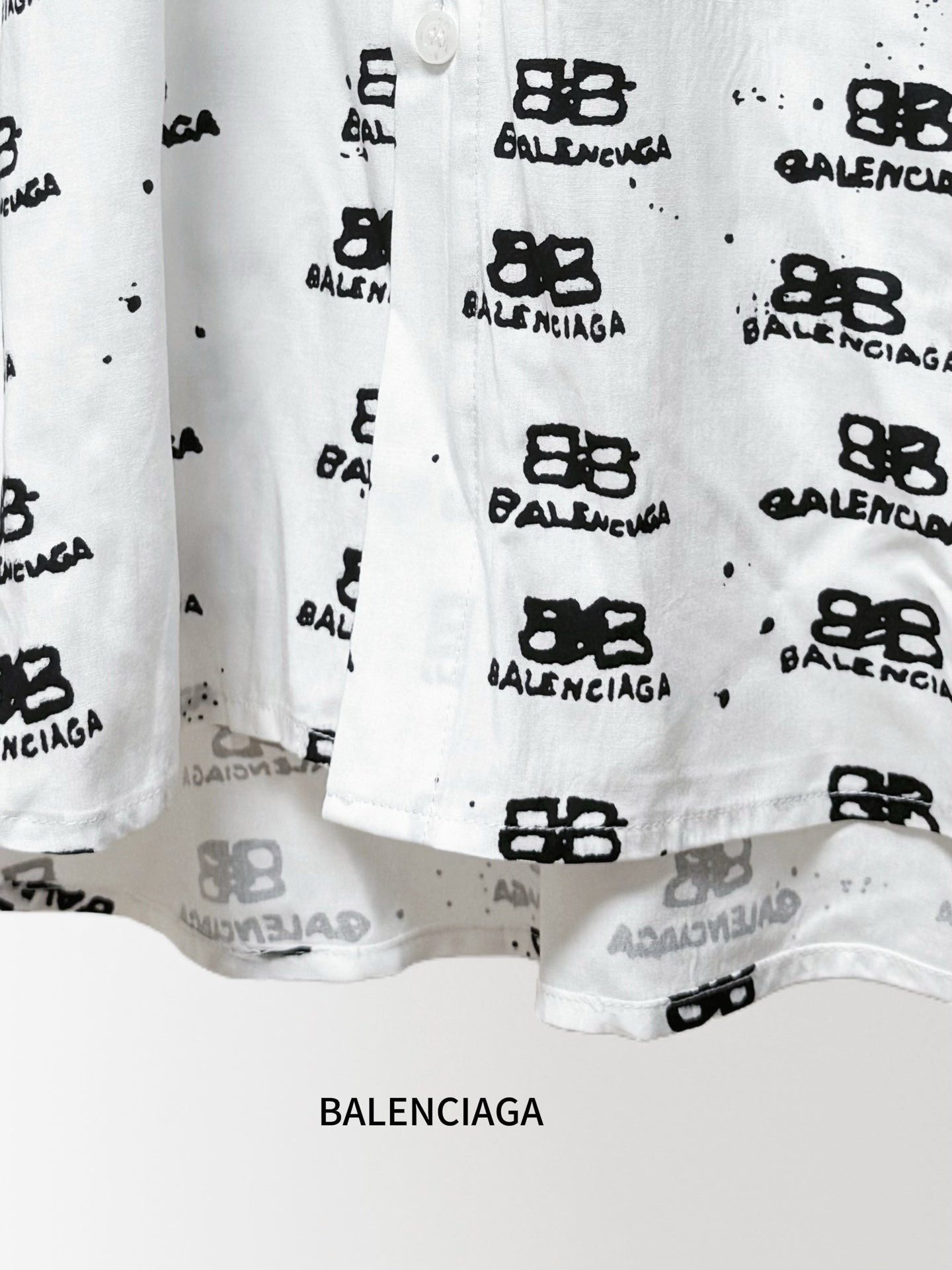 Balenciaga long-sleeve shirt hem close-up in white with black logo pattern and buttons
