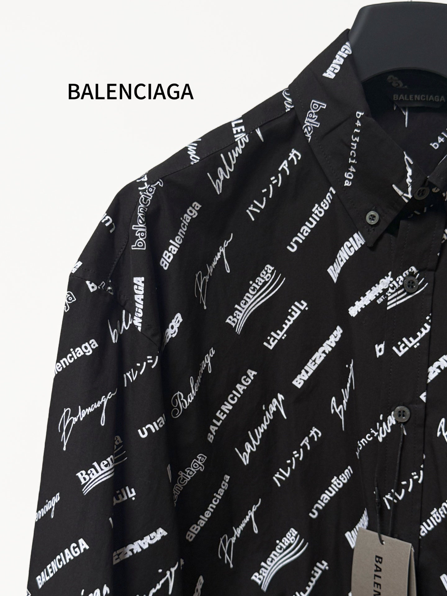 Black long-sleeve button-up shirt with repeating white script logo pattern, shoulder close-up
