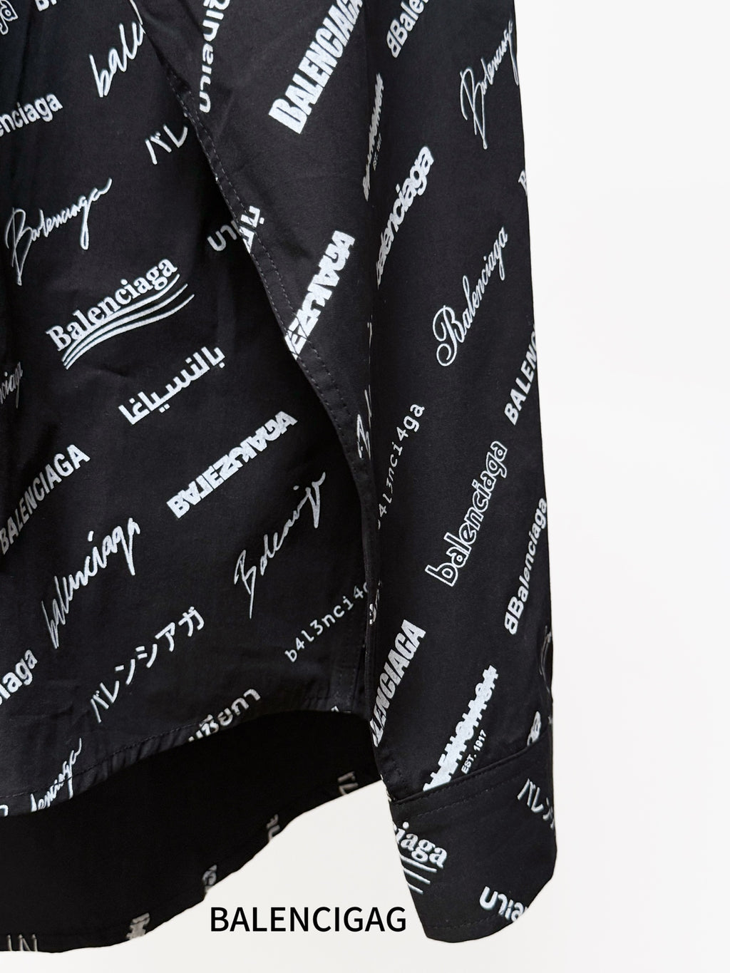 Black long-sleeve button-up shirt with repeating white script logo pattern, side seam close-up