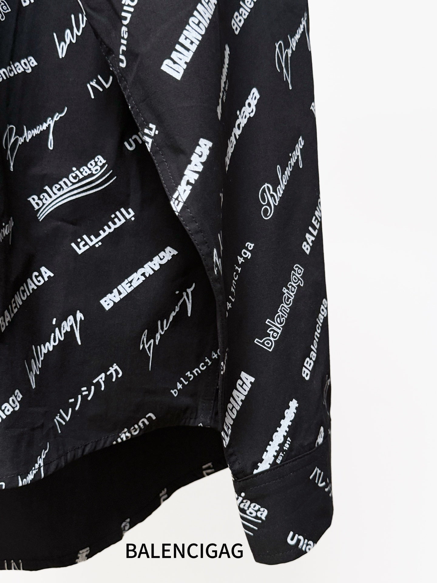 Black long-sleeve button-up shirt with repeating white script logo pattern, side seam close-up