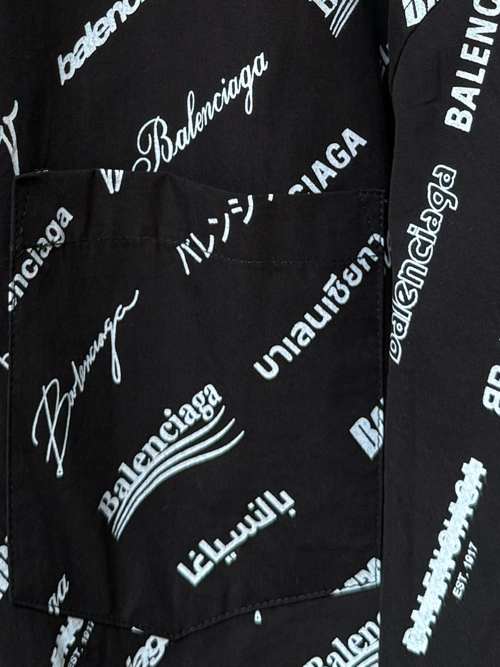 Black long-sleeve button-up shirt with repeating white script logo pattern, pocket area close-up