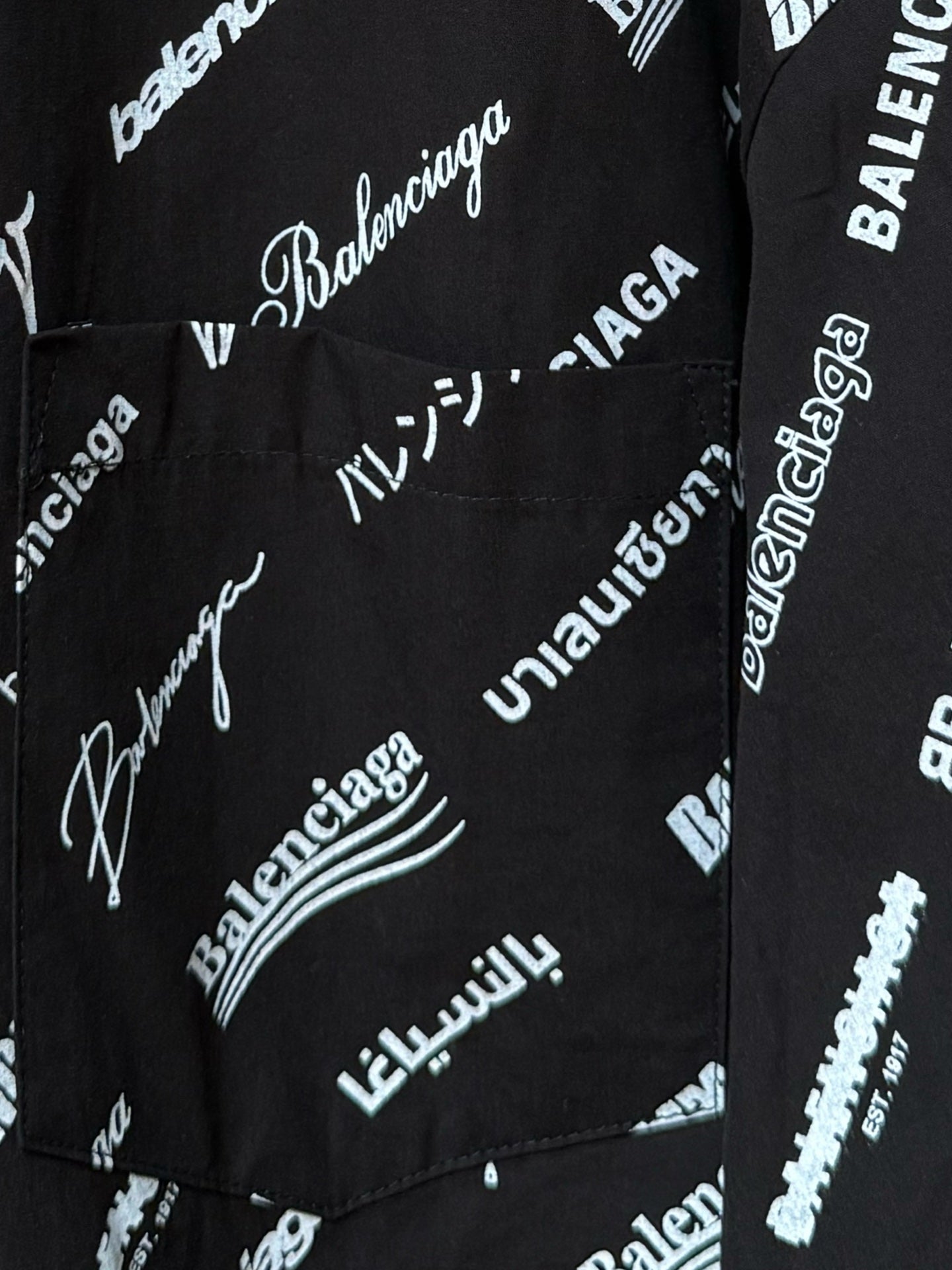 Black long-sleeve button-up shirt with repeating white script logo pattern, pocket area close-up