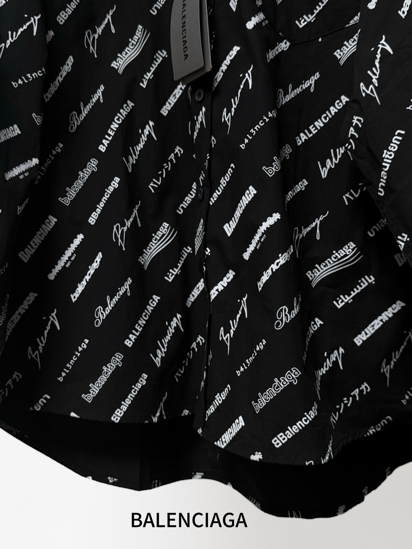Black long-sleeve button-up shirt with repeating white script logo pattern, lower hem close-up