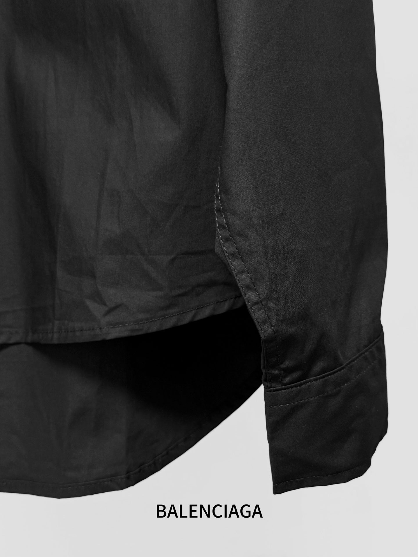 Long-sleeve button-up shirt by Balenciaga, dark black, lower side hem and drape.