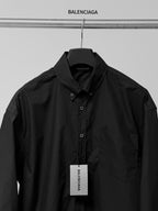 Long-sleeve button-up shirt by Balenciaga, dark black, collar and buttons with hanging tag.