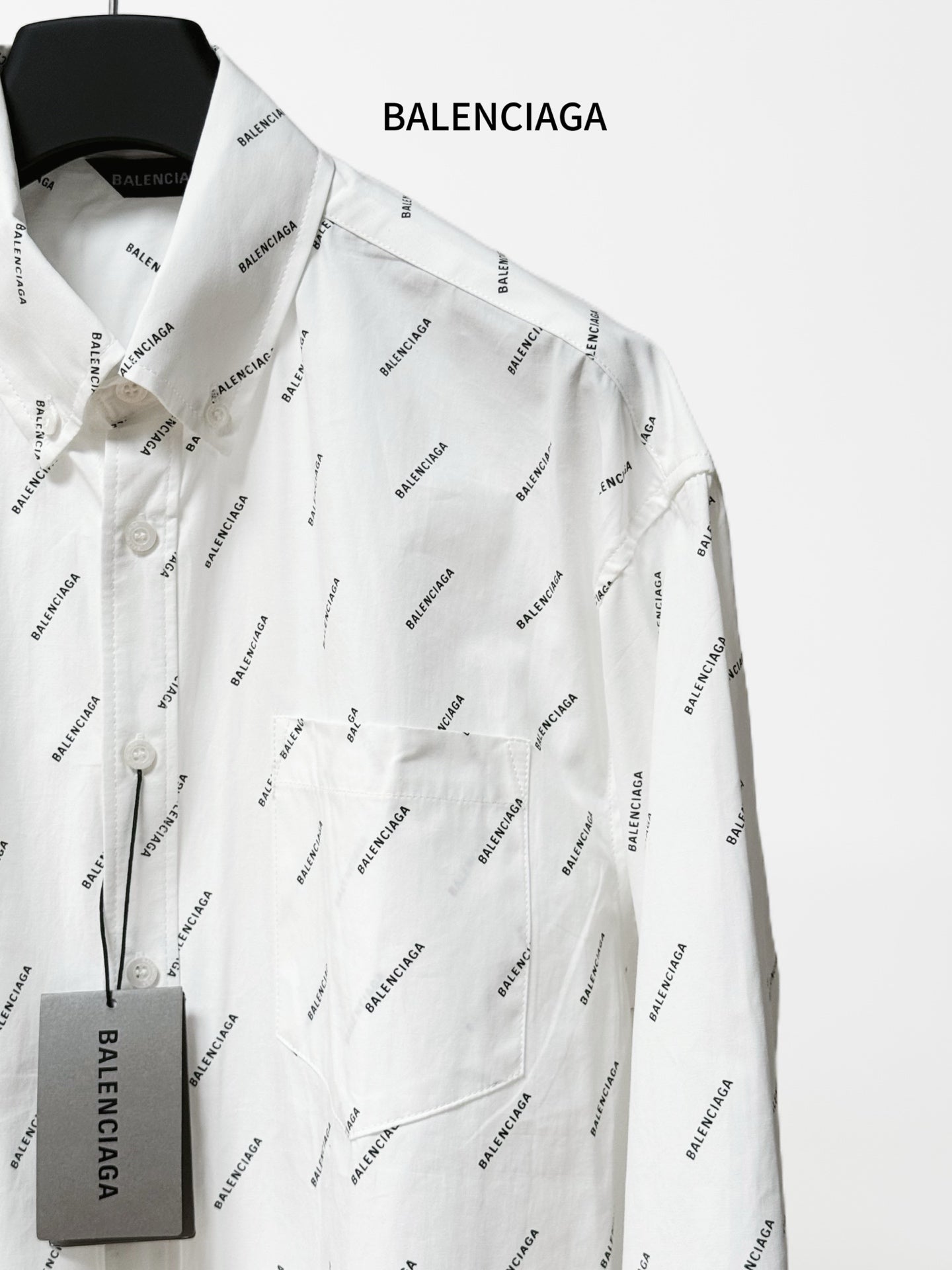 Long-sleeve button-up shirt with black logo pattern, chest pocket and hanging tag