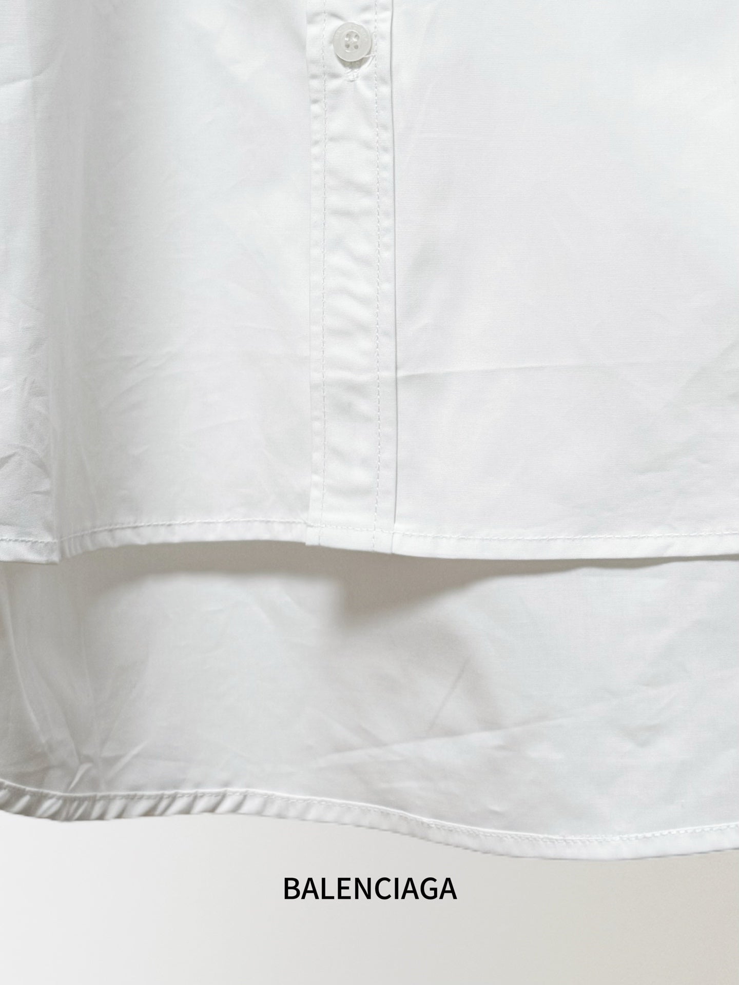 White Balenciaga button-up shirt hem with pleats and a row of visible buttons
