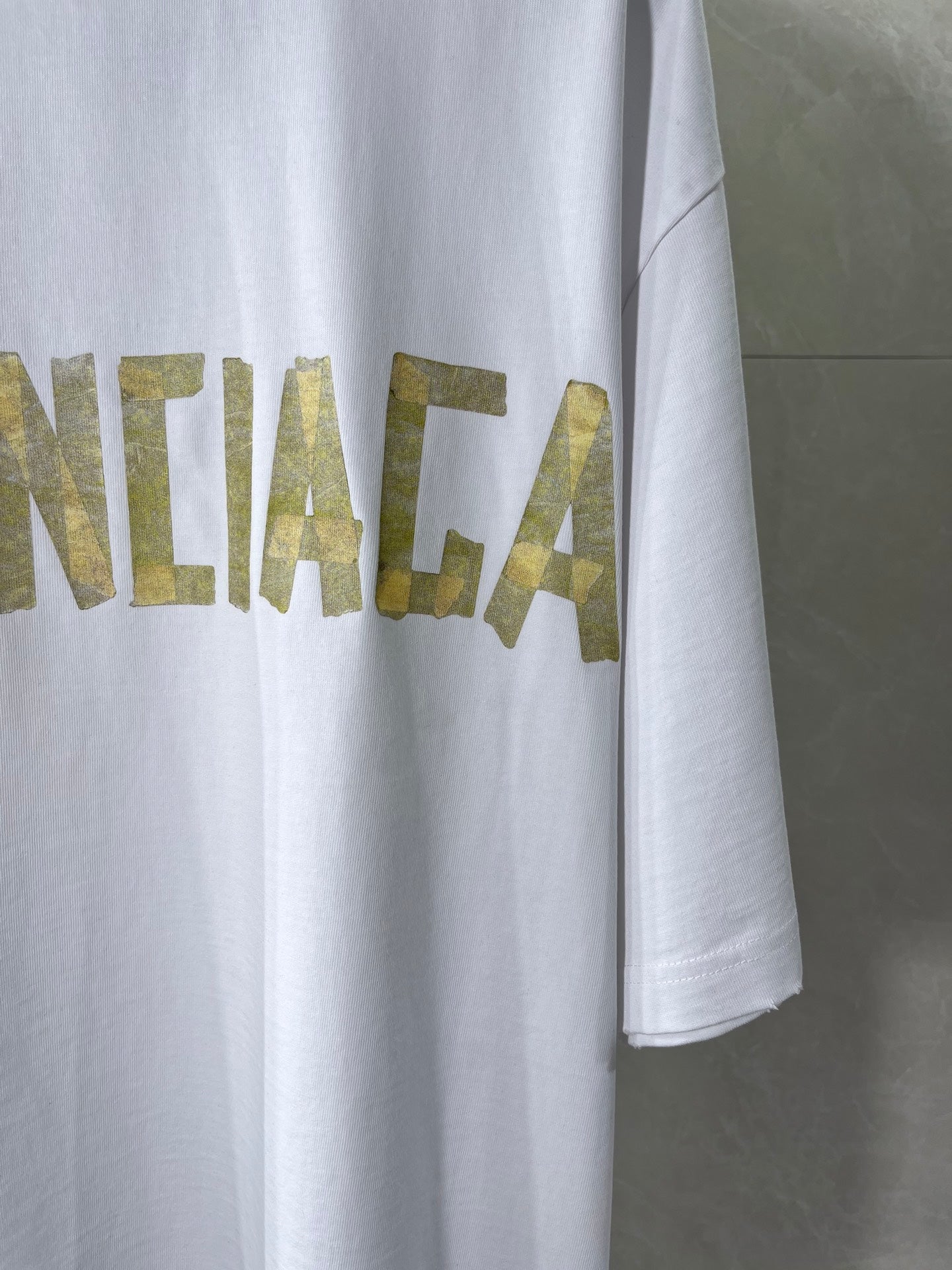 White Balenciaga T-shirt with partial gold text graphic on chest and side hem