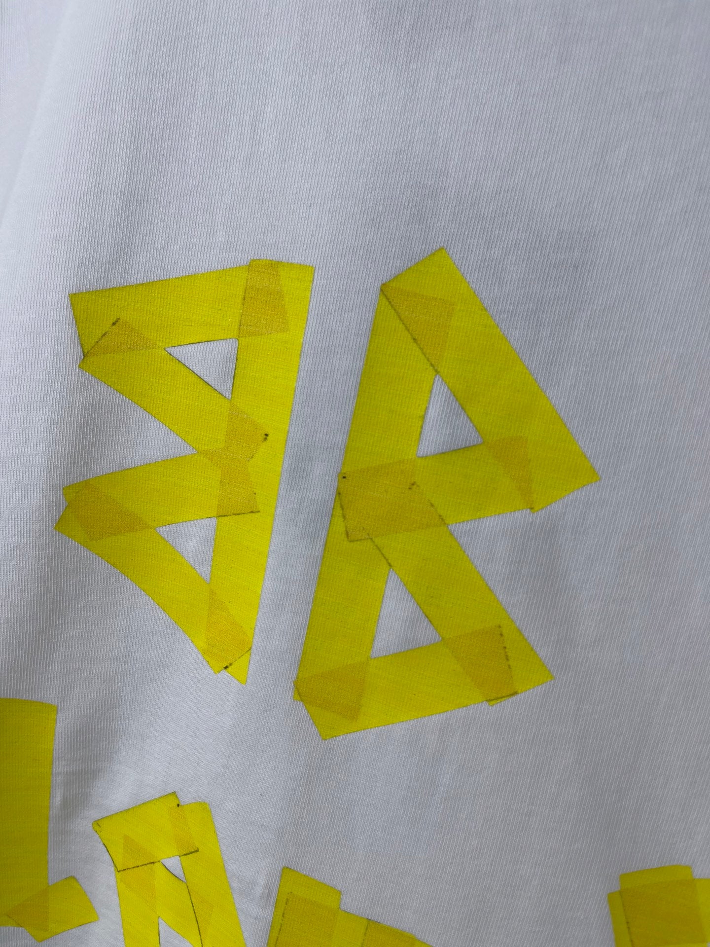 White Balenciaga T-shirt close-up of bright yellow BA lettering graphic