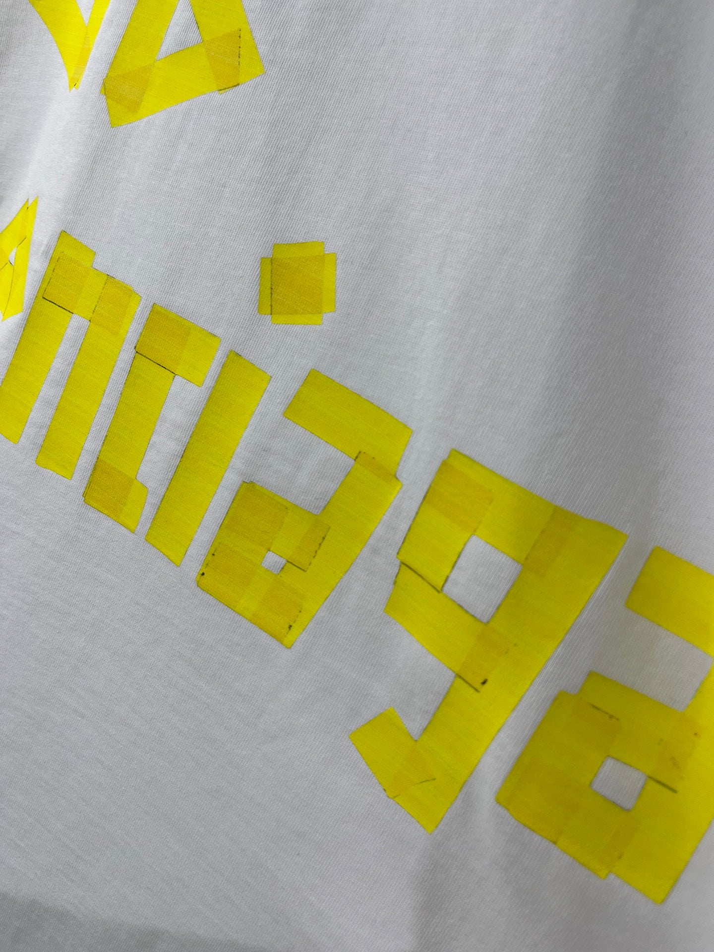 White Balenciaga T-shirt close-up of yellow graphic text across fabric