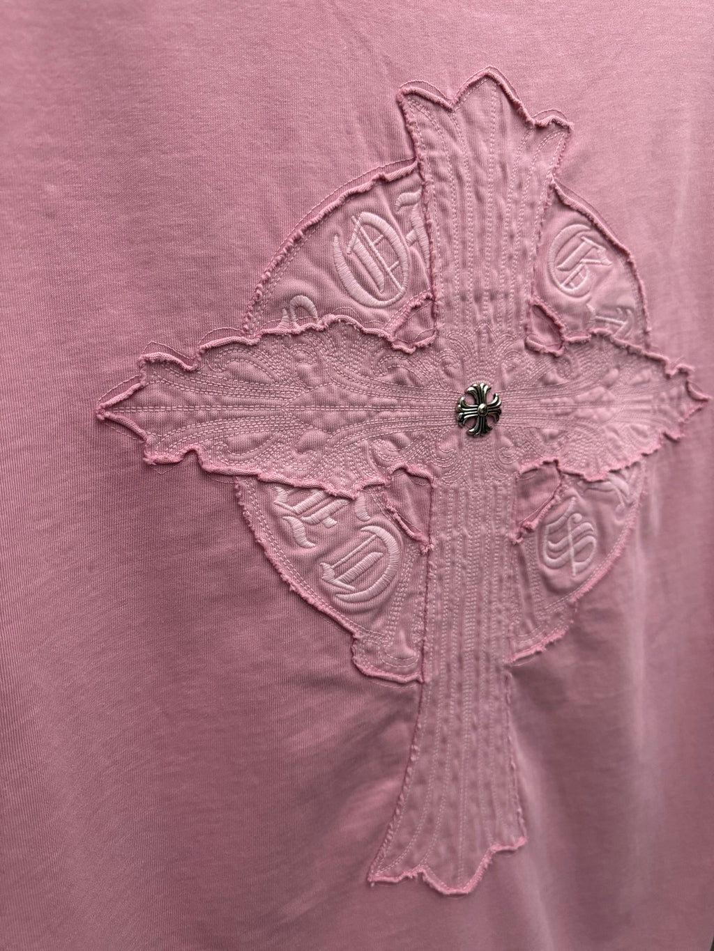 Pink T-shirt close-up of raised cross emblem with stitched symbols