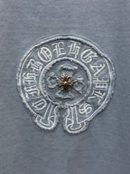 Round crest embroidery close-up on light blue T-shirt with gold center detail