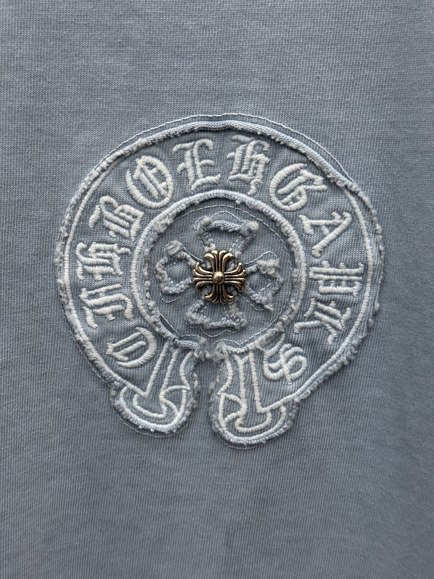 Round crest embroidery close-up on light blue T-shirt with gold center detail