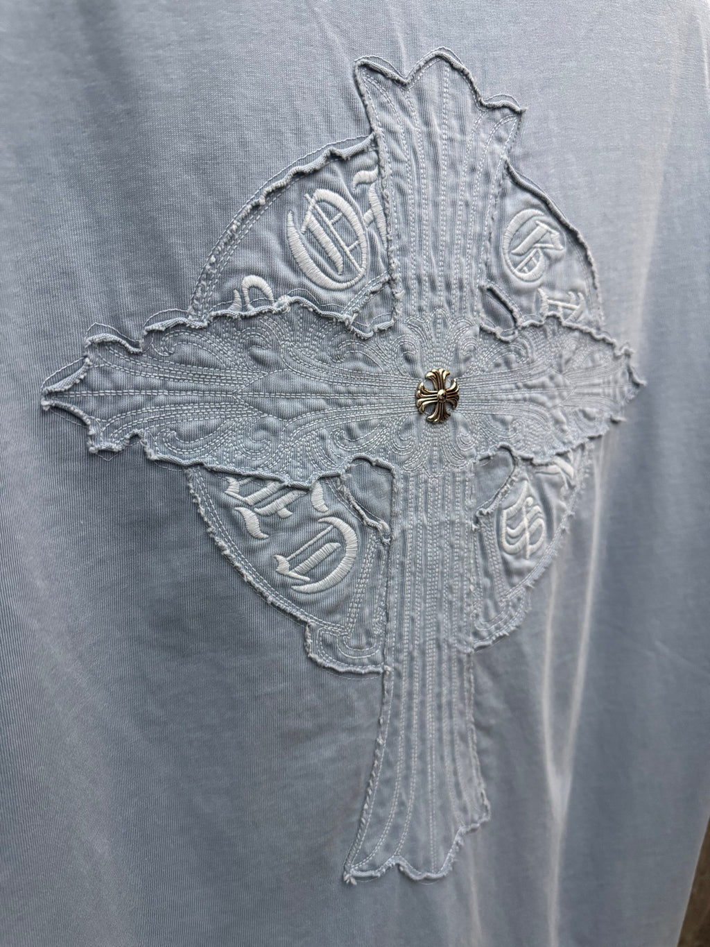 Close-up of large crest embroidery on light blue T-shirt back, with gold pin
