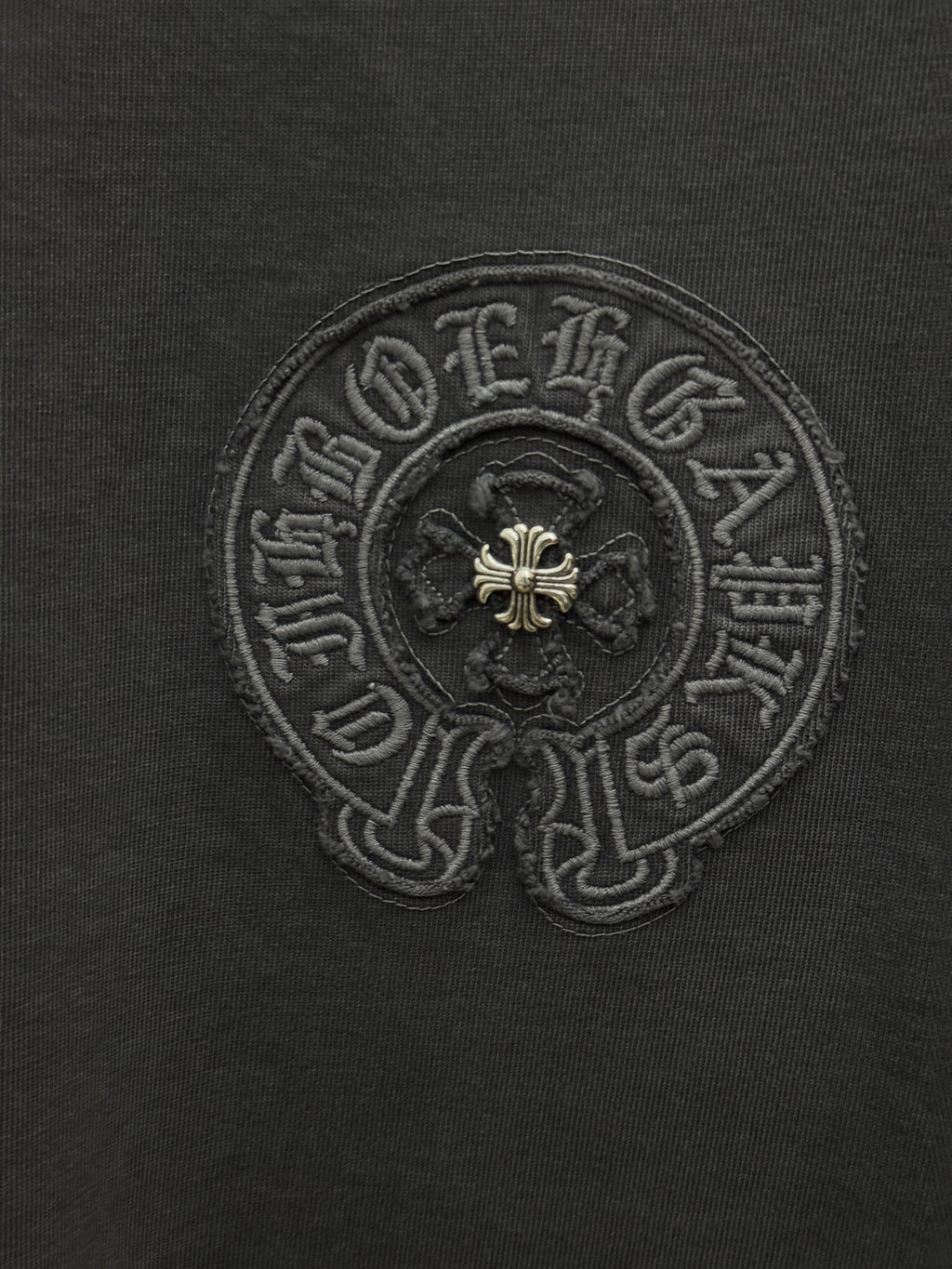 Dark gray T-shirt close-up of embroidered circular crest with fleur-de-lis