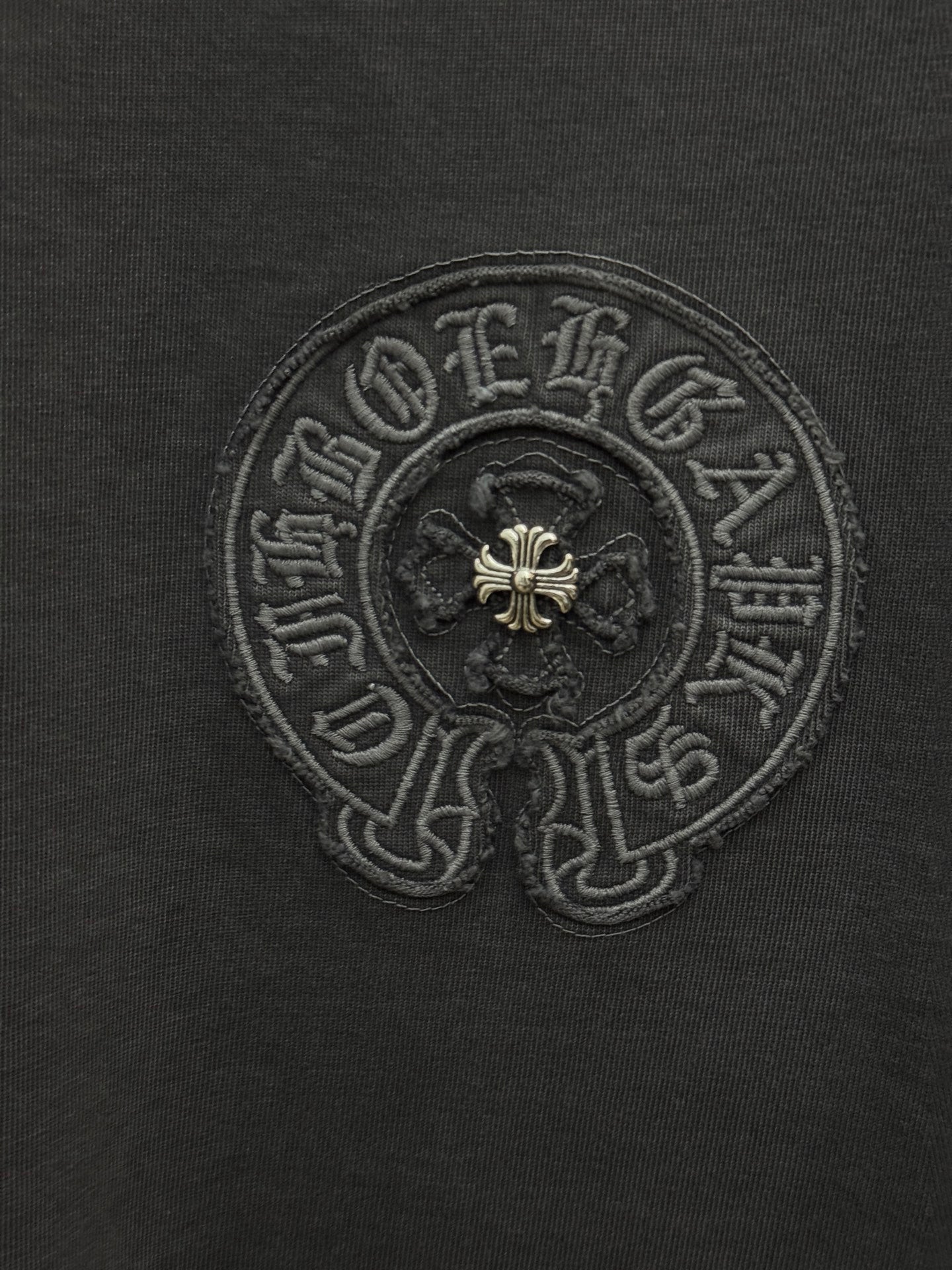 Dark gray T-shirt close-up of embroidered circular crest with fleur-de-lis
