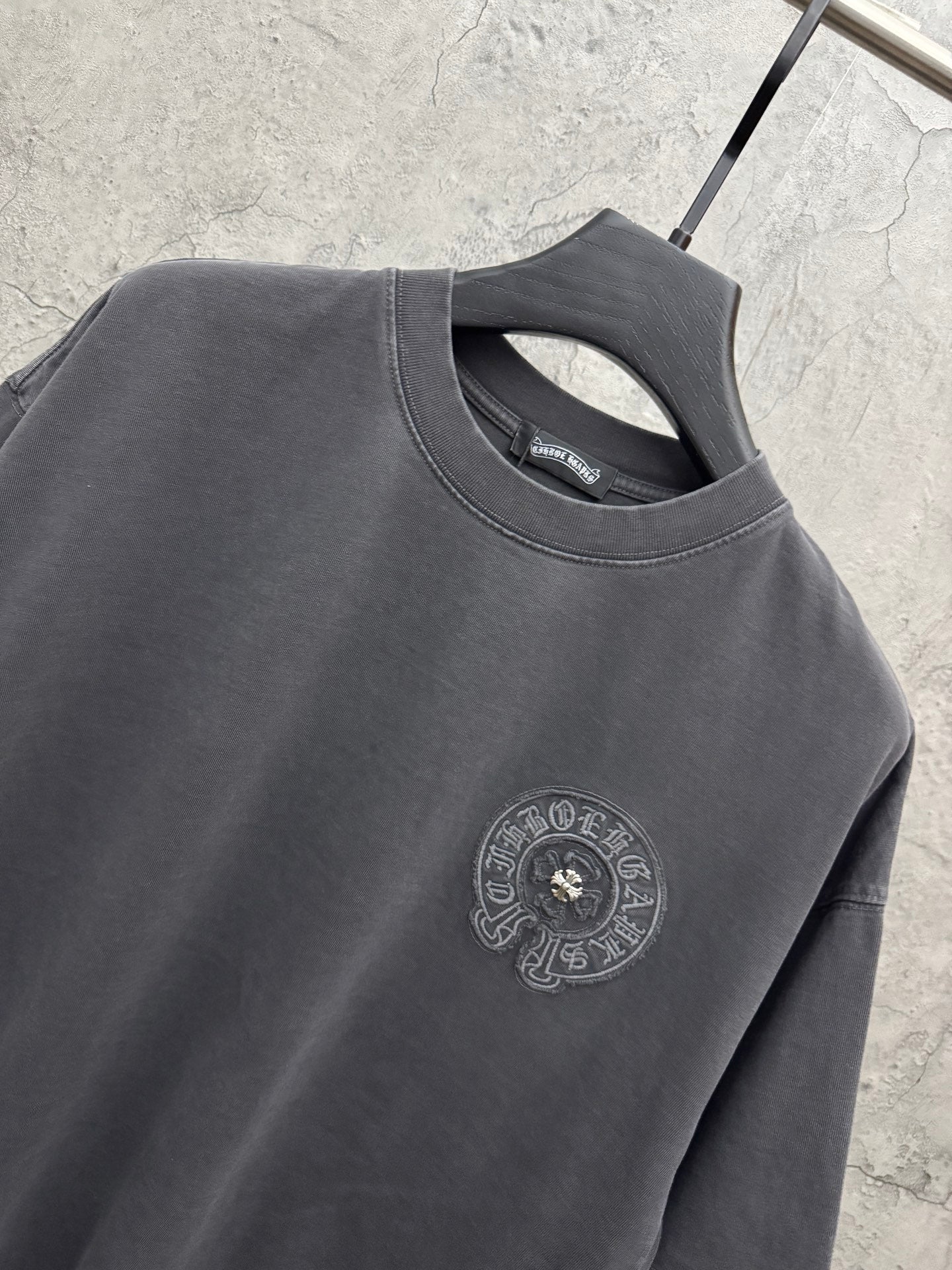 Dark gray crew-neck T-shirt neckline with small circular embroidered chest crest