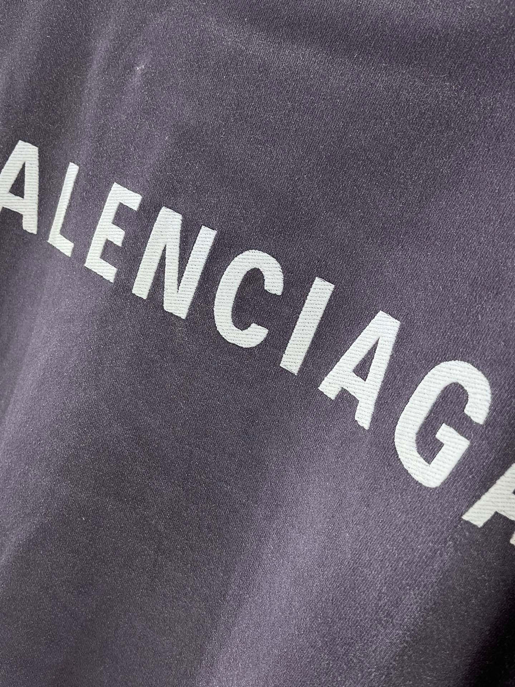 BALENCIAGA logo text on dark purple T-shirt fabric, close-up
