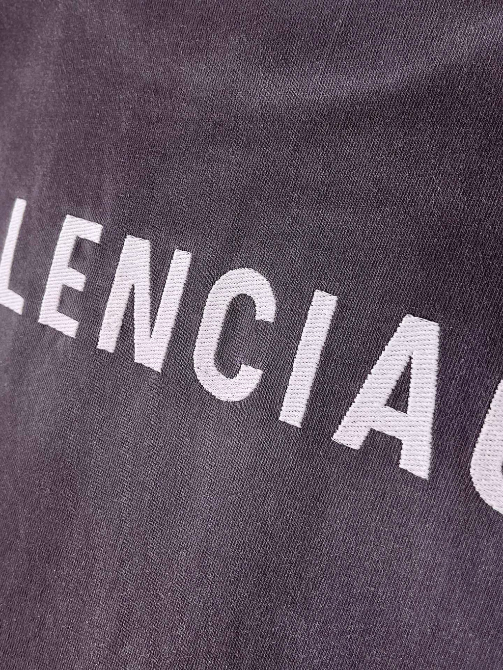 BALENCIAGA logo text on dark purple T-shirt fabric, close-up