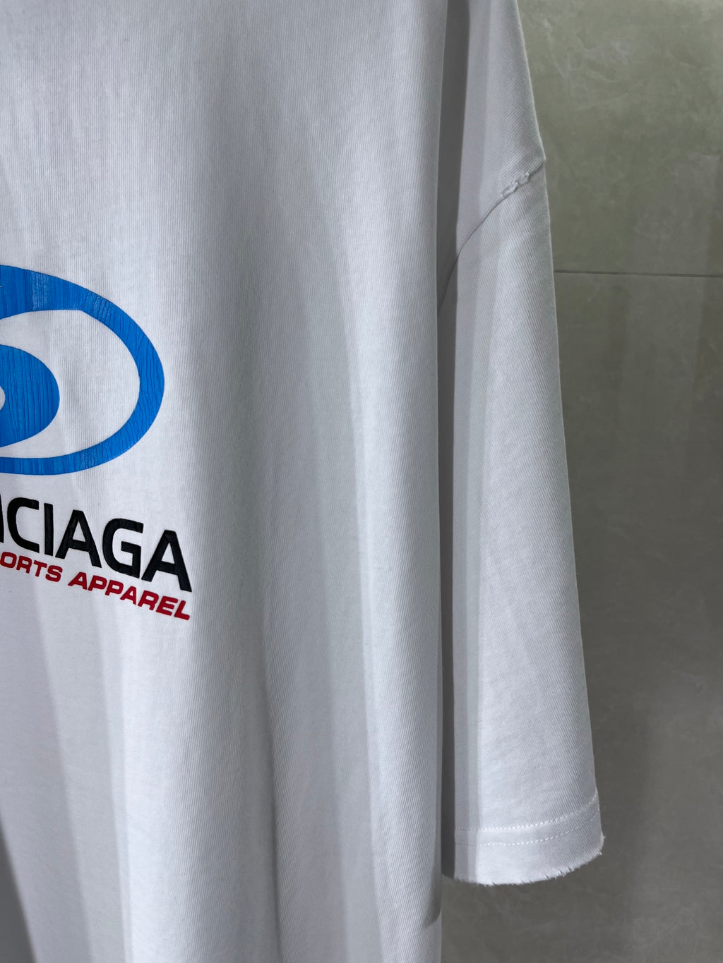 Balenciaga white T-shirt sleeve with partial blue logo and red text