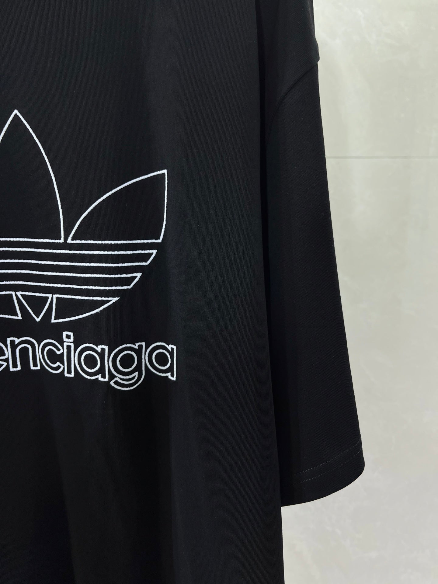 Balenciaga T-shirt sleeve and side graphic with white trefoil logo on dark fabric
