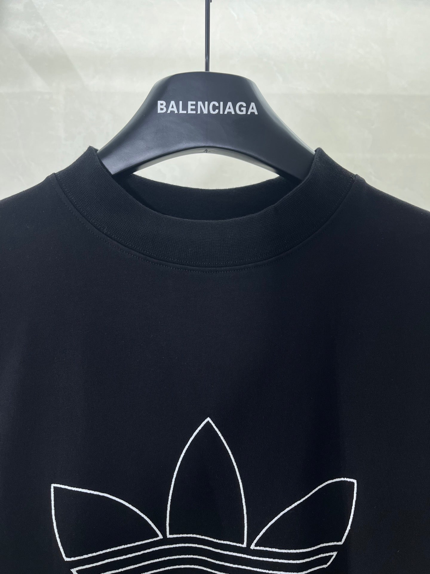 Balenciaga T-shirt neckline with white trefoil graphic outline on dark fabric