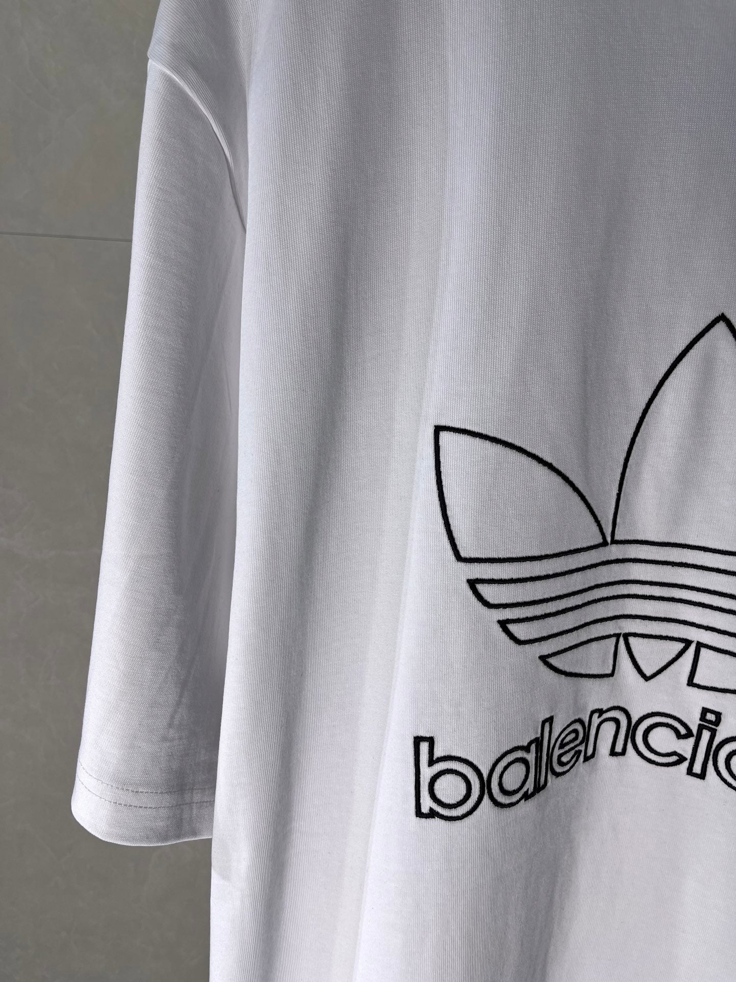 White Balenciaga logo T-shirt, side close-up of trefoil emblem and printed text.