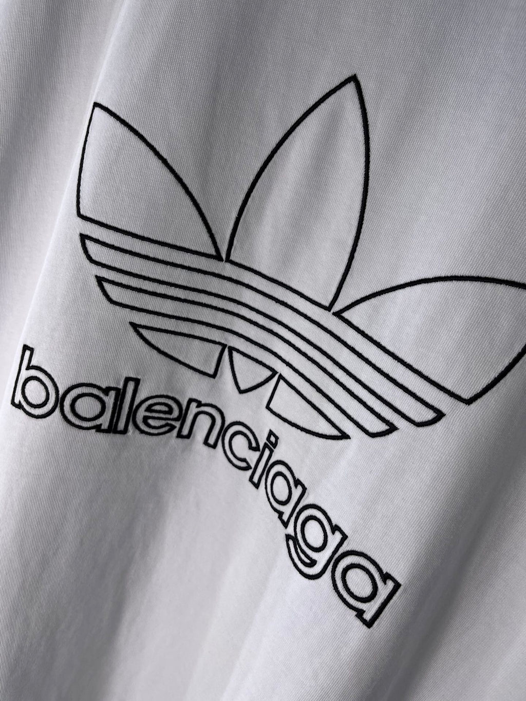 White Balenciaga logo T-shirt, detailed view of trefoil graphic and “balenciaga” text.