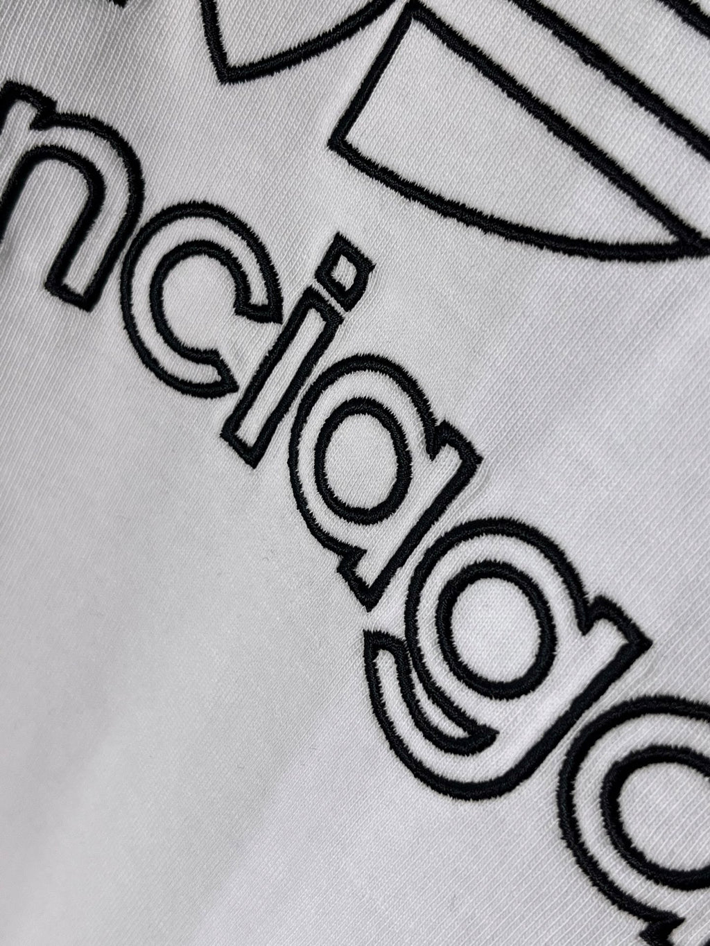 White Balenciaga logo T-shirt, close-up of “balenciaga” lettering with outline design.