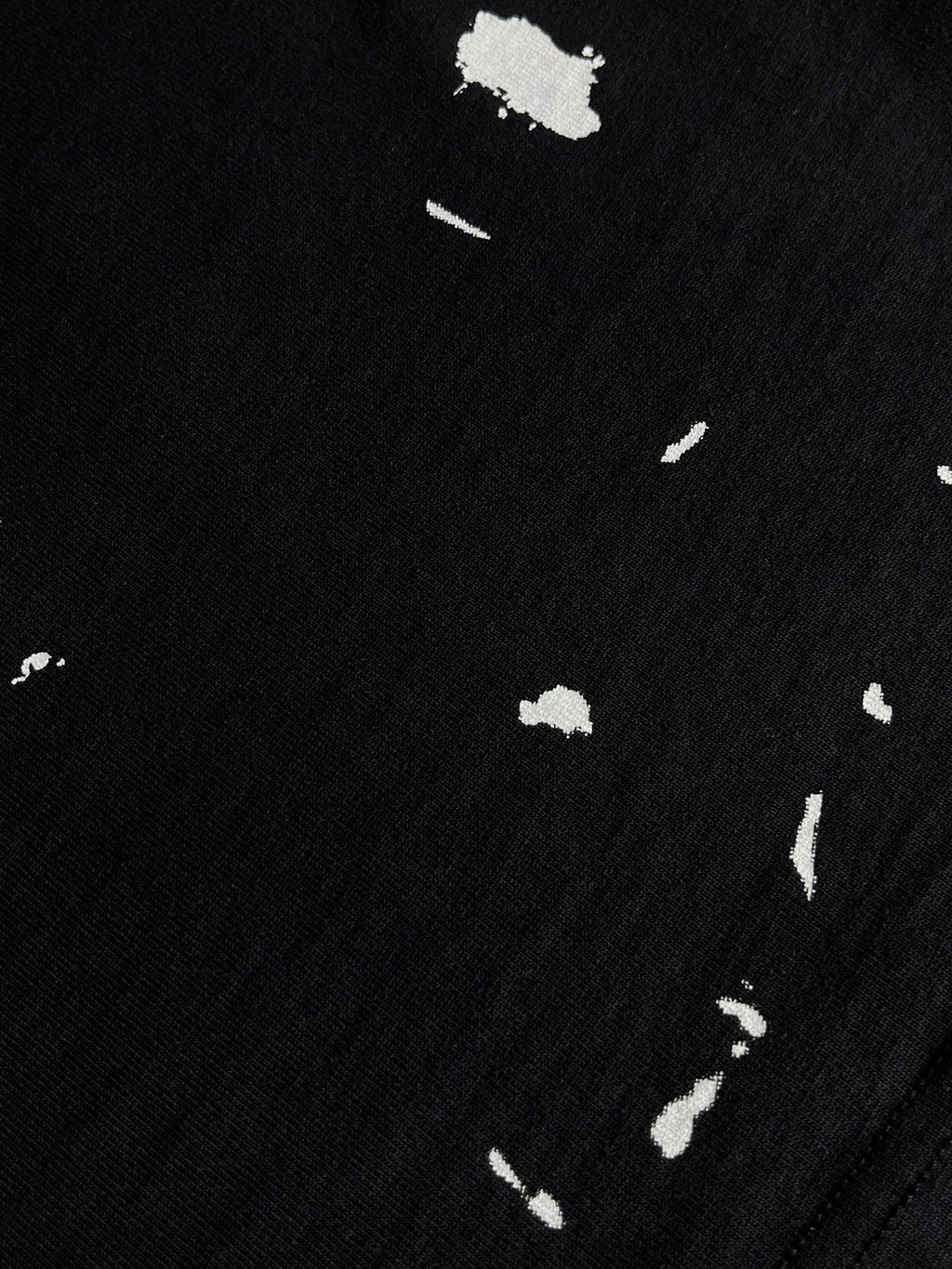 Dark T-shirt fabric close-up with white paint-like speckles