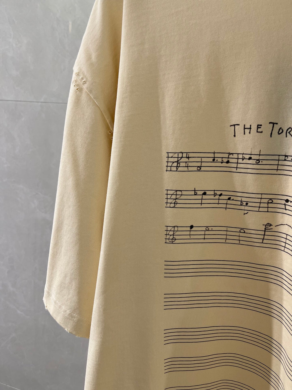 Balenciaga cream T-shirt sleeve detail with musical staff graphic