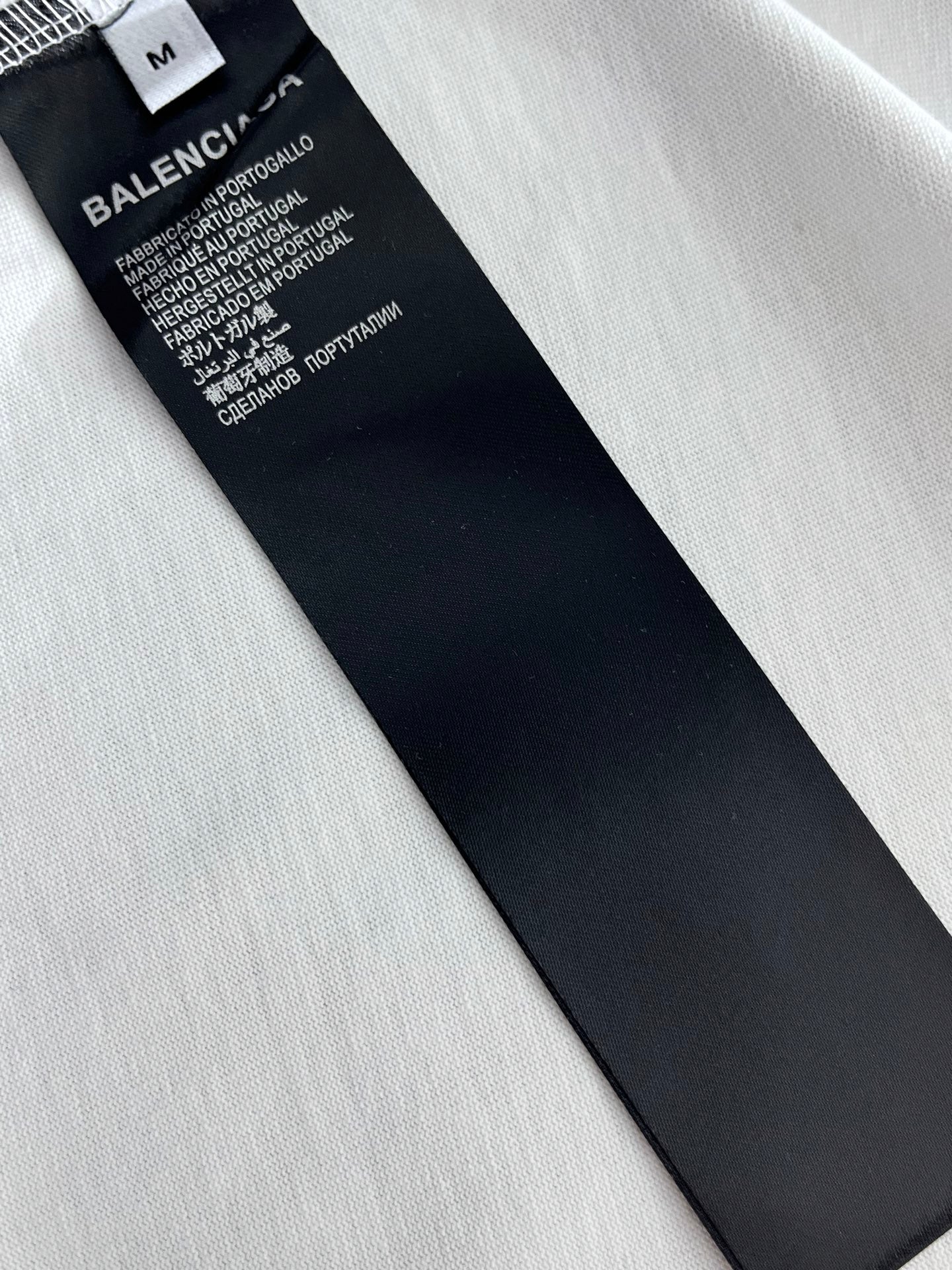 Black size label and care text on white T-shirt fabric, angled view