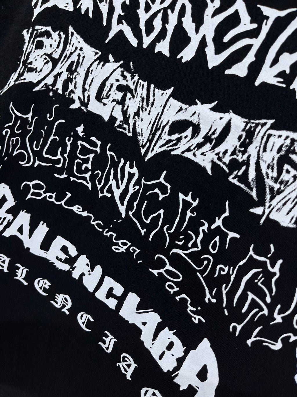 Balenciaga T-shirt pattern close-up, black with scattered white wordmark-style print