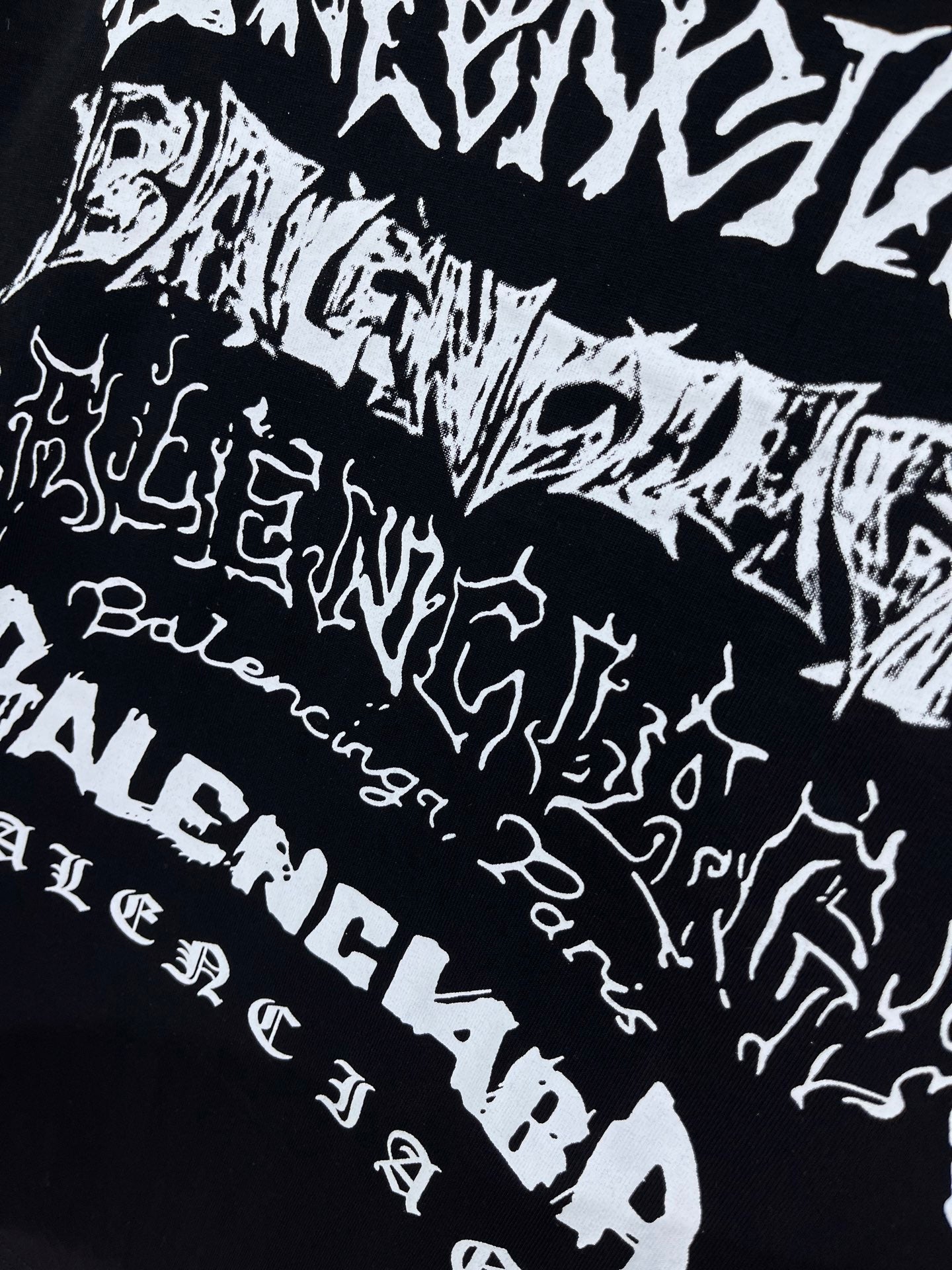 Balenciaga T-shirt pattern close-up, black with scattered white wordmark-style print