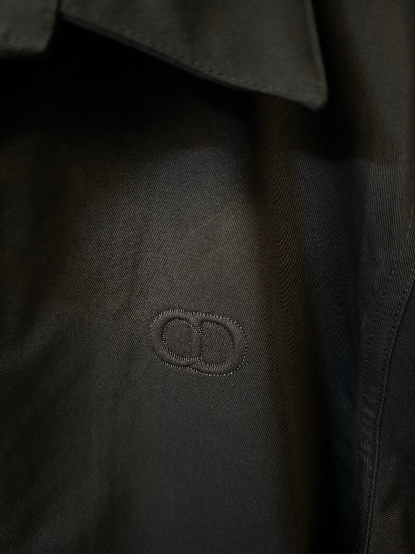 Dark navy jacket chest emblem in outlined logo, close-up