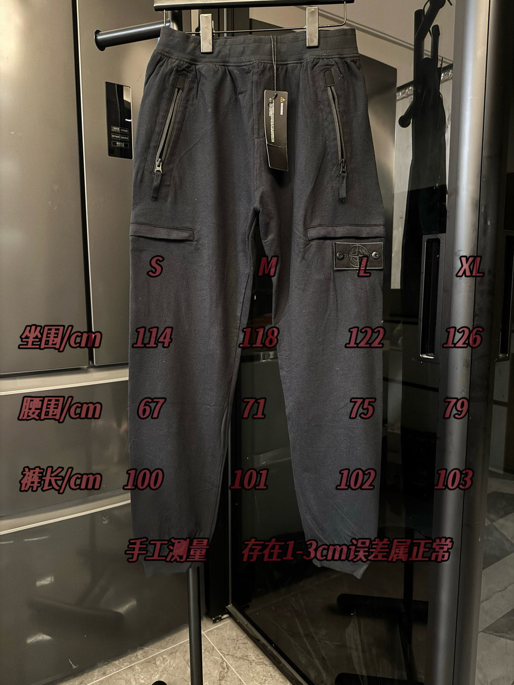 Stone Island cargo trousers on display, dark gray with drawstring and size markers on glass