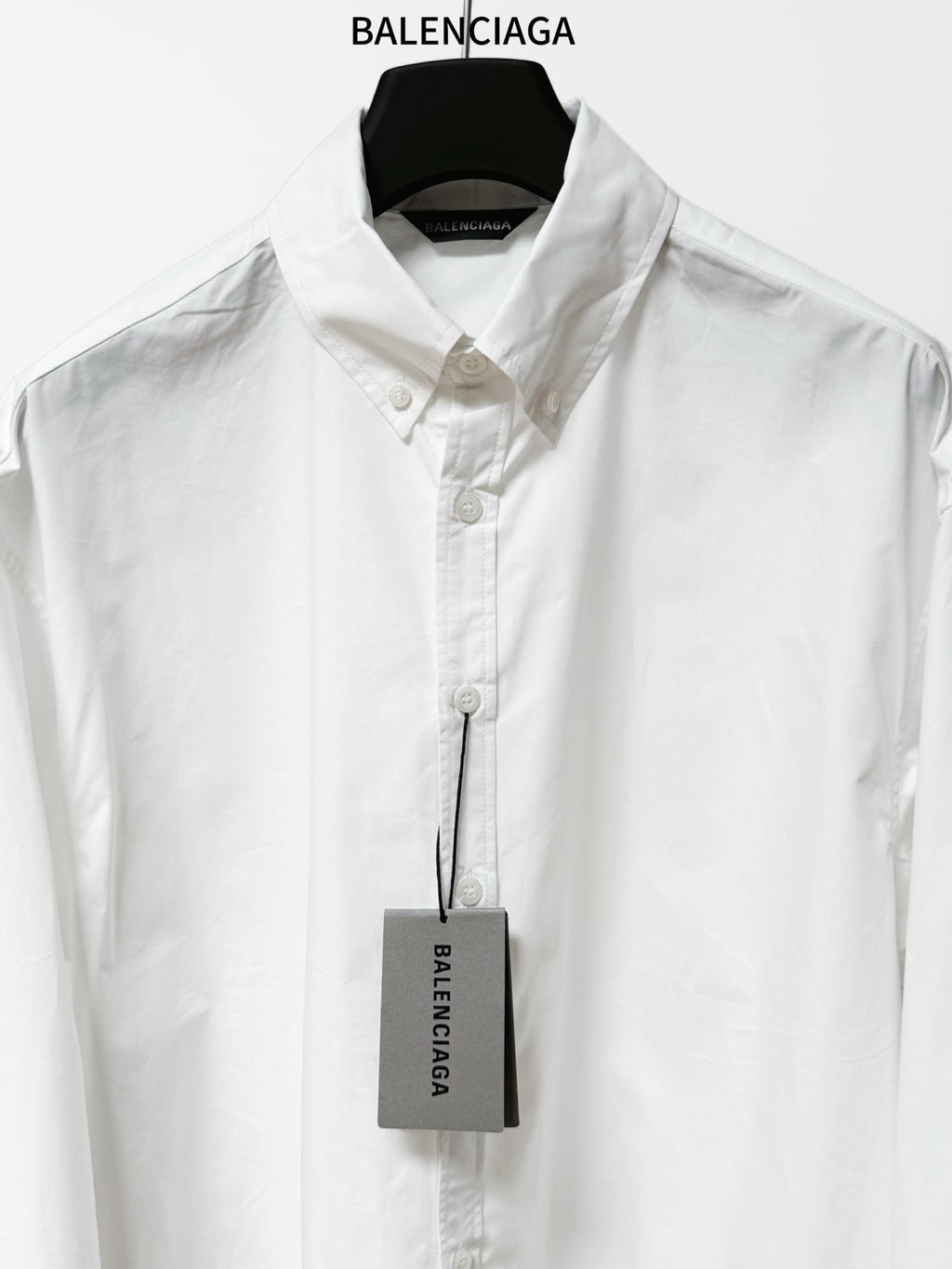 White button-up shirt with pointed collar, front button placket, hanging product tag