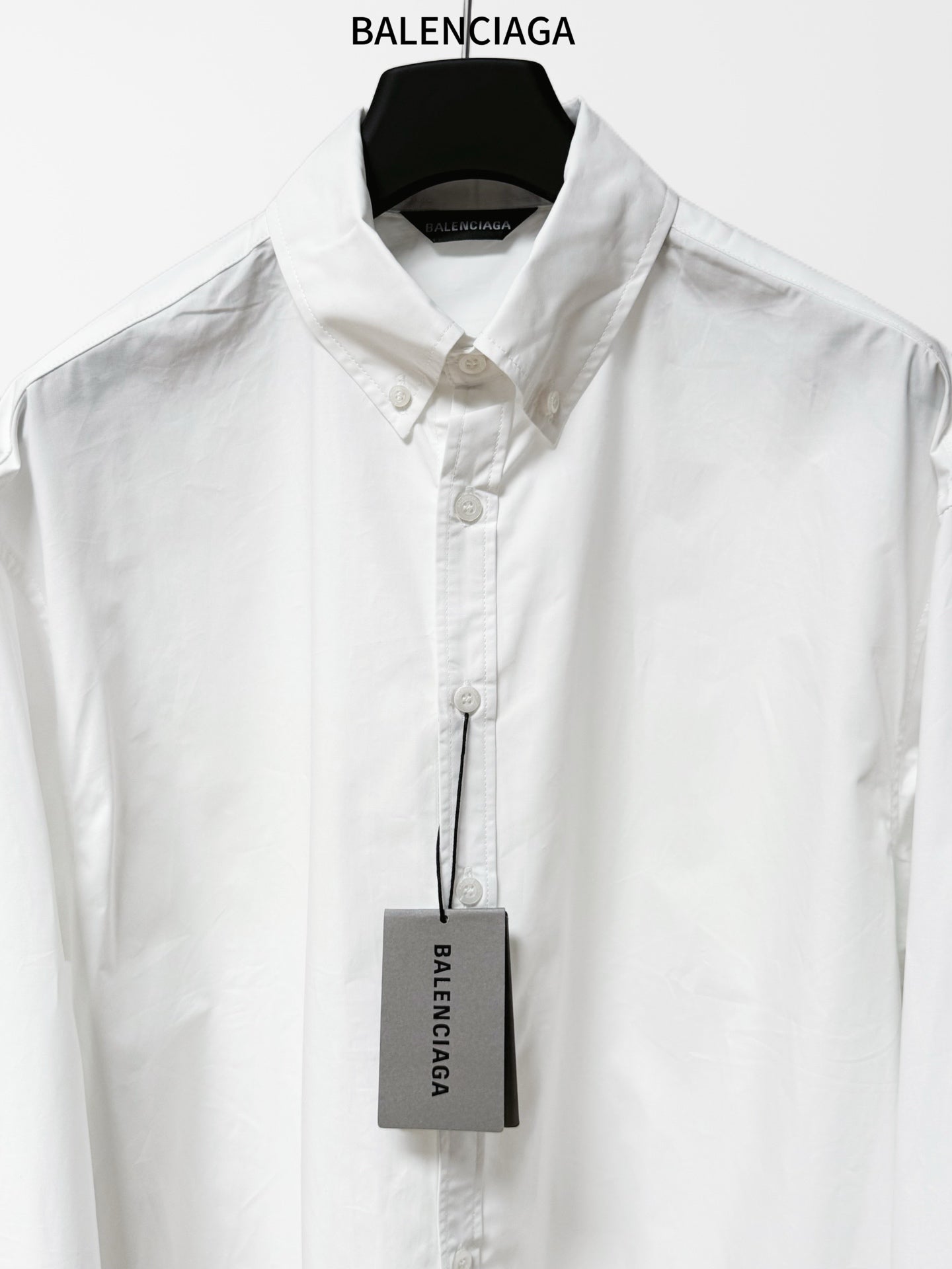 White button-up shirt with pointed collar, front button placket, hanging product tag