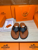 Black leather thong sandals with H logo straps and tan-brown soles.