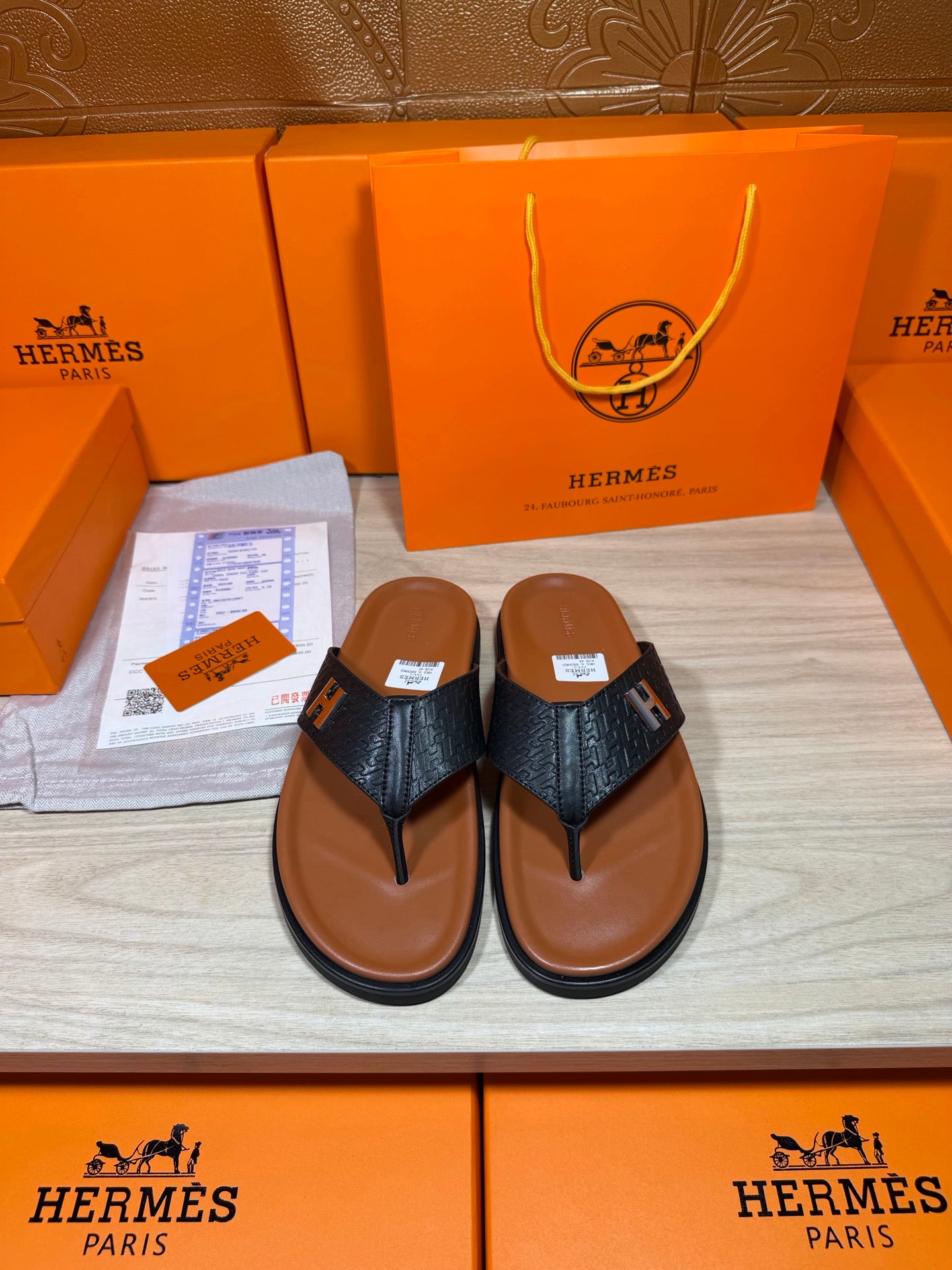 Black leather thong sandals with H logo straps and tan-brown soles.